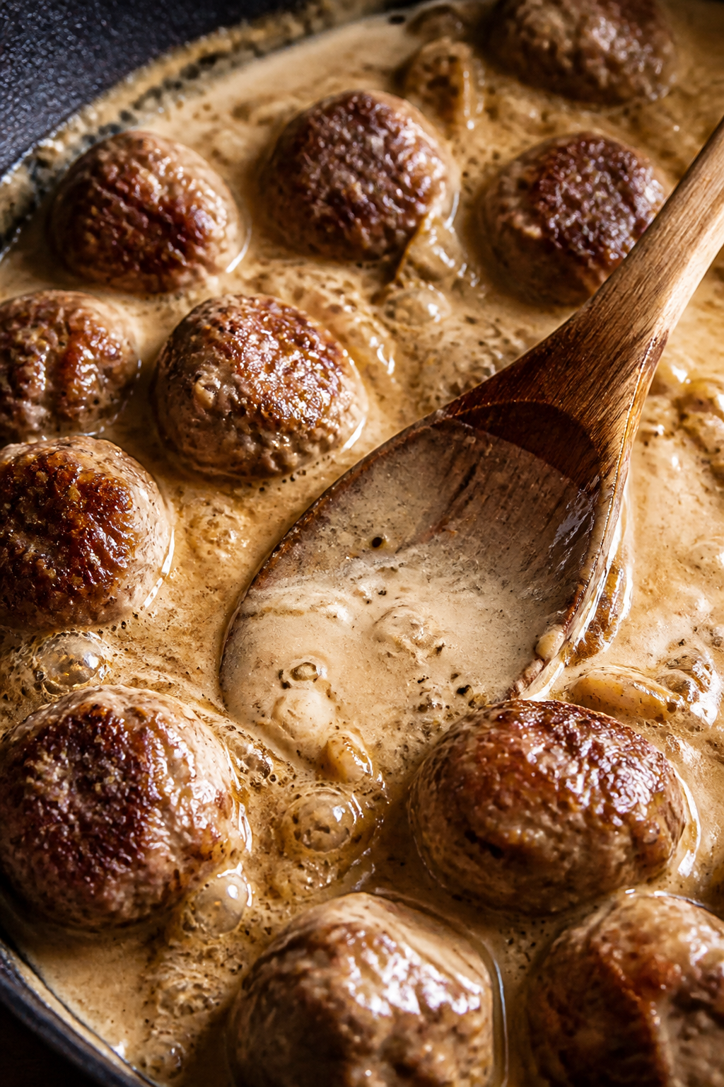 Close-up detail: A skillet of browned Swedish meatballs simmering in silky keto cream gravy, steam r
