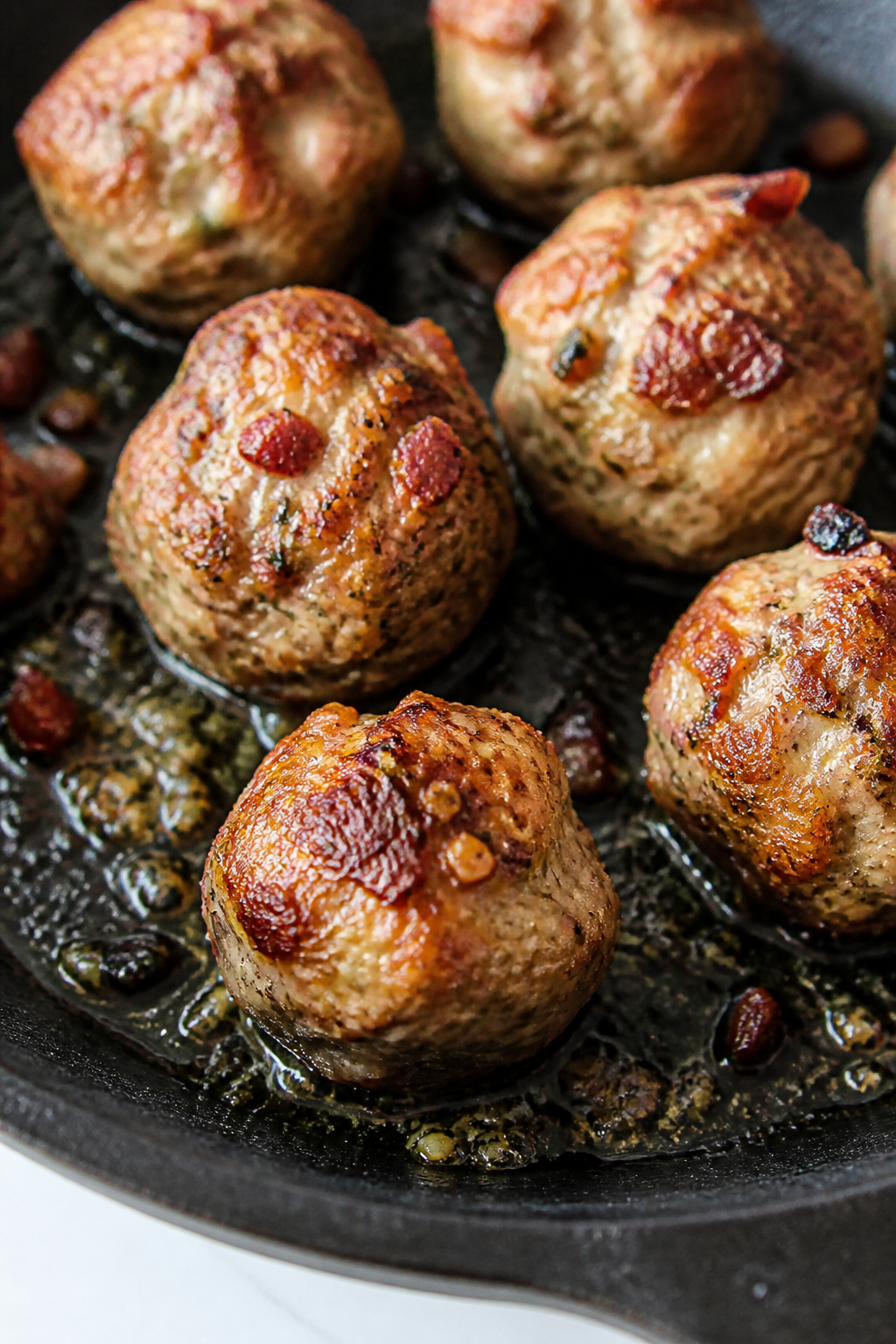 Close-up detail: Searing chicken bacon meatballs in a skillet, golden-brown crust with rendered baco