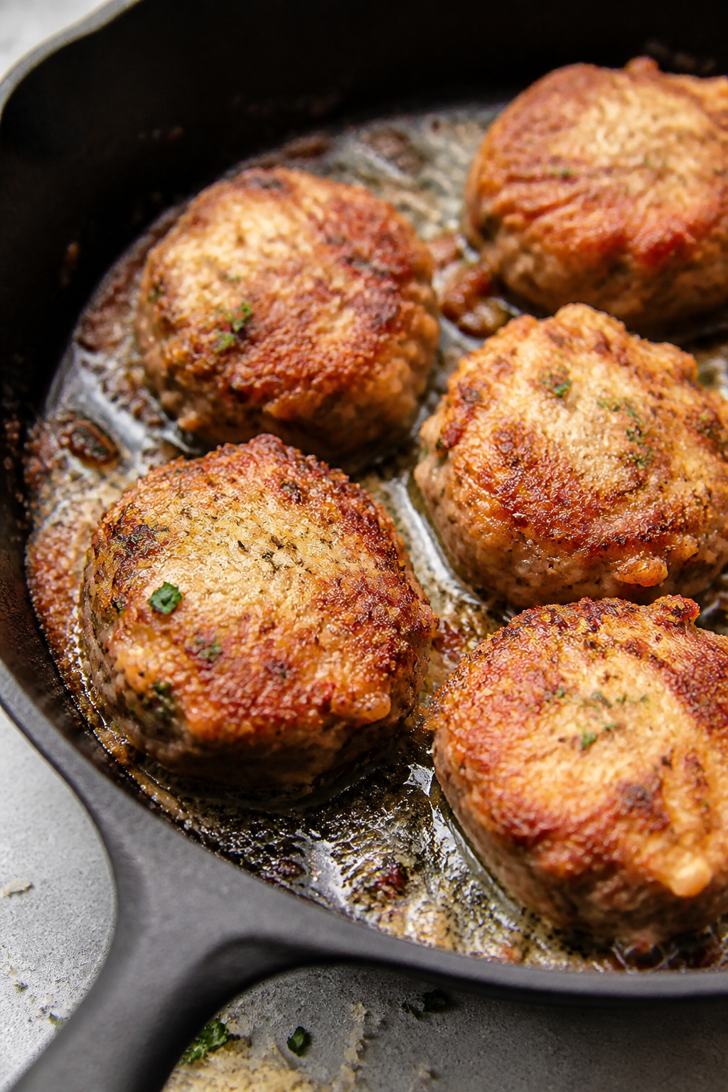 Close-up detail: Searing Keto Parmesan Crusted Meatballs in a cast-iron skillet, golden Parmesan cru
