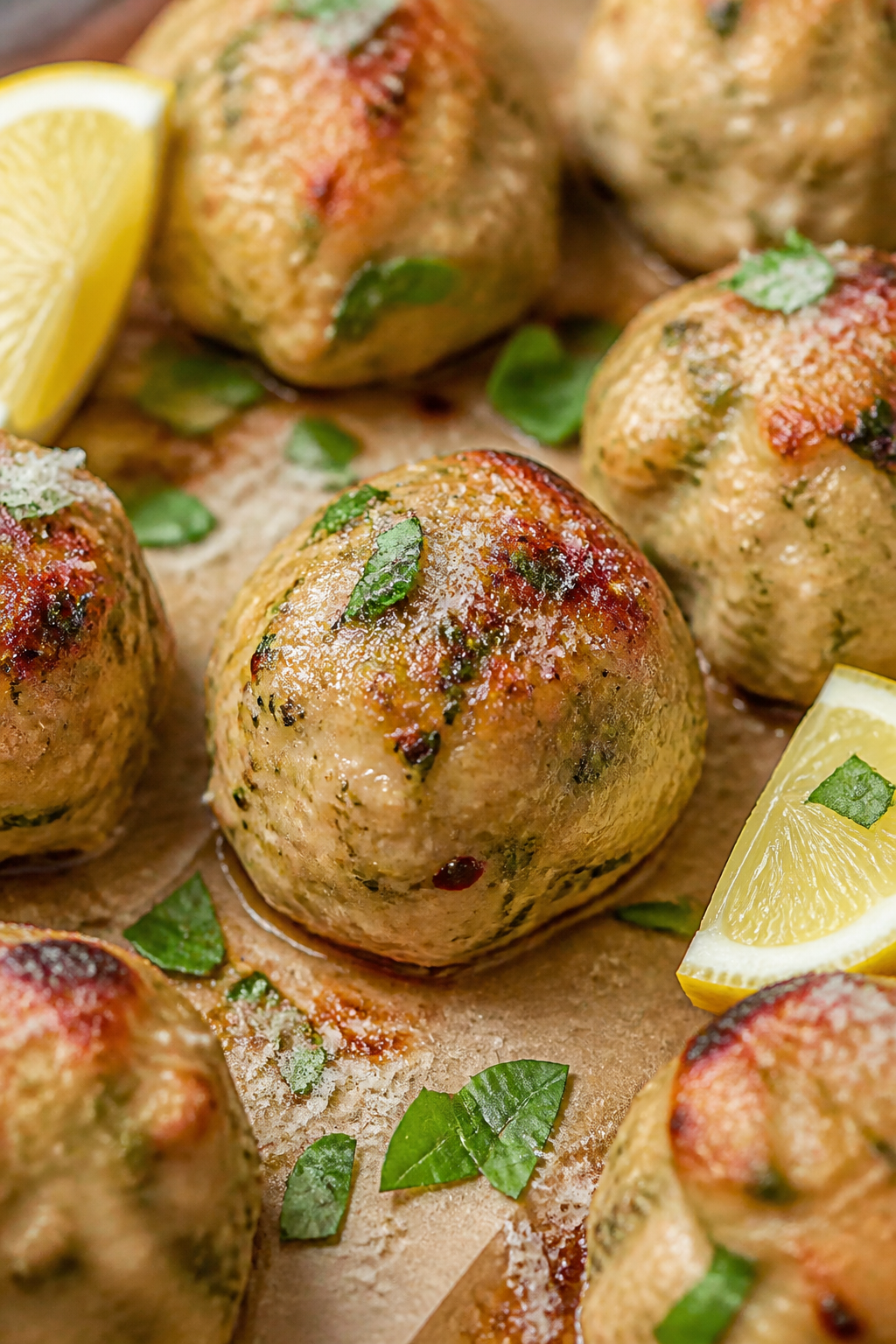 Close-up detail shot: Juicy baked keto pesto chicken meatballs just out of the oven on a parchment-l