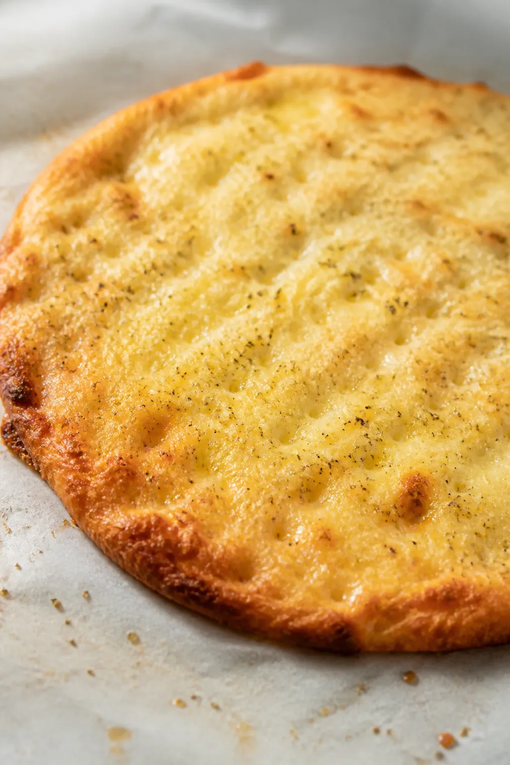 Close-up detail: Golden par-baked keto “fathead” crust on parchment, edges lightly blistered and