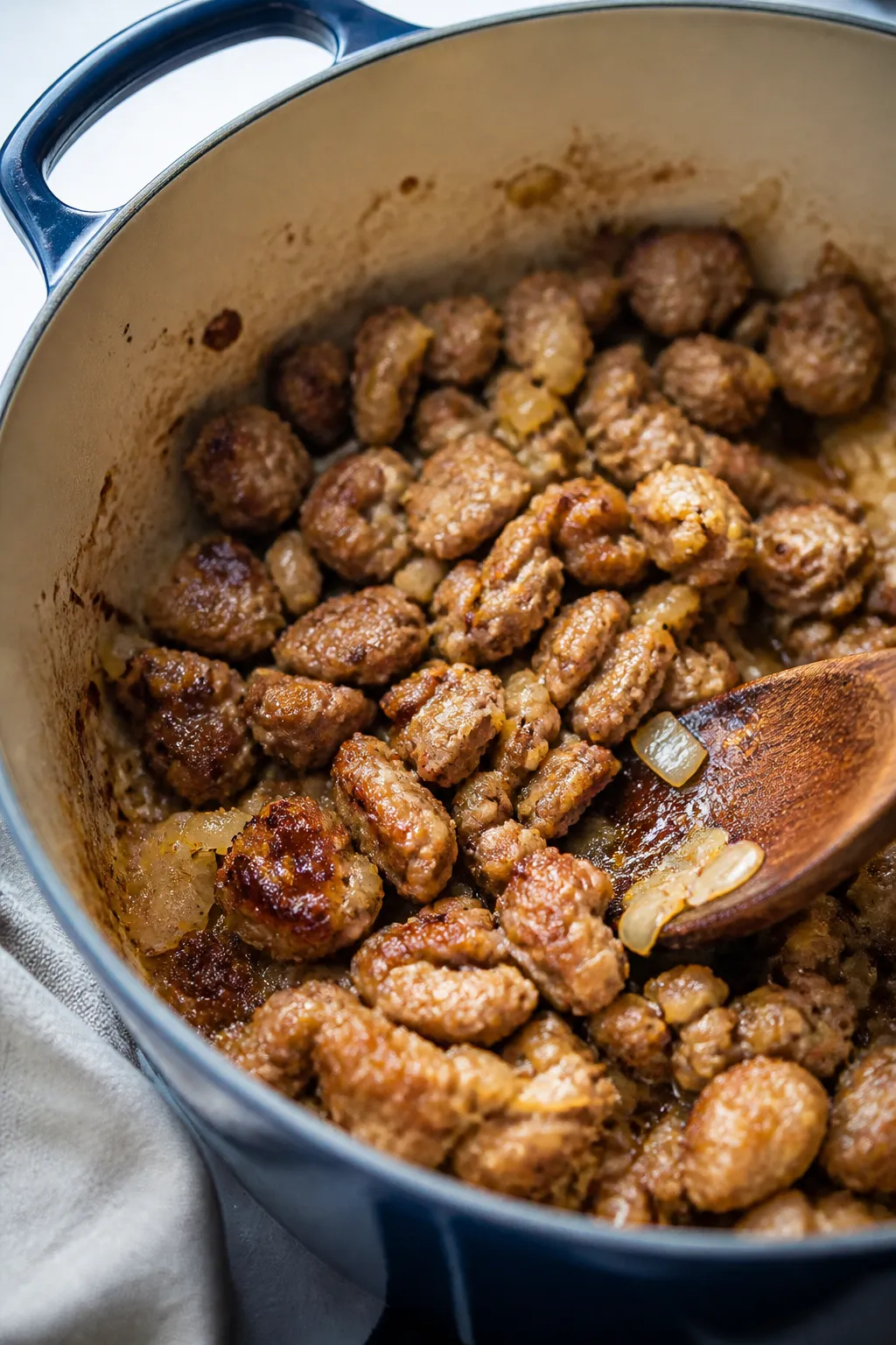 Cooking process close-up: Italian sausage browning in a Dutch oven with translucent sautéed onions 