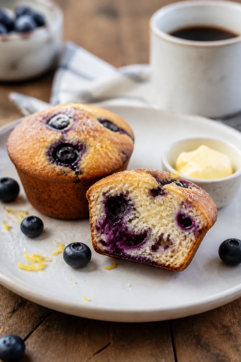Final plated presentation: two keto blueberry muffins on a matte white plate, one muffin halved to s